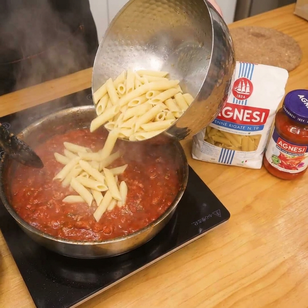 Penne werden zur Tomaten-Speck-Soße in die Pfanne gegeben.