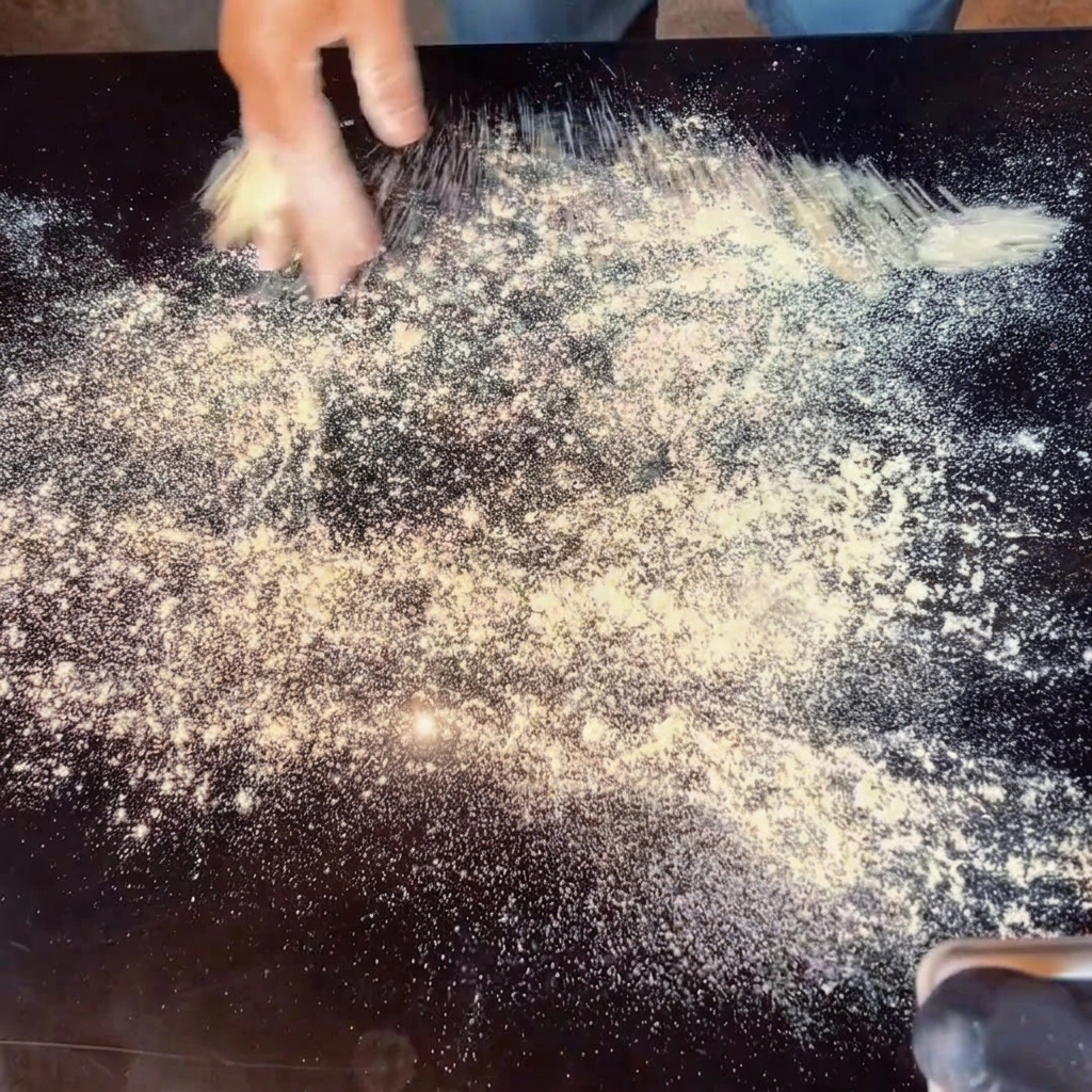 Hände, die Pizzateig auf einer bemehlten Oberfläche dehnen.