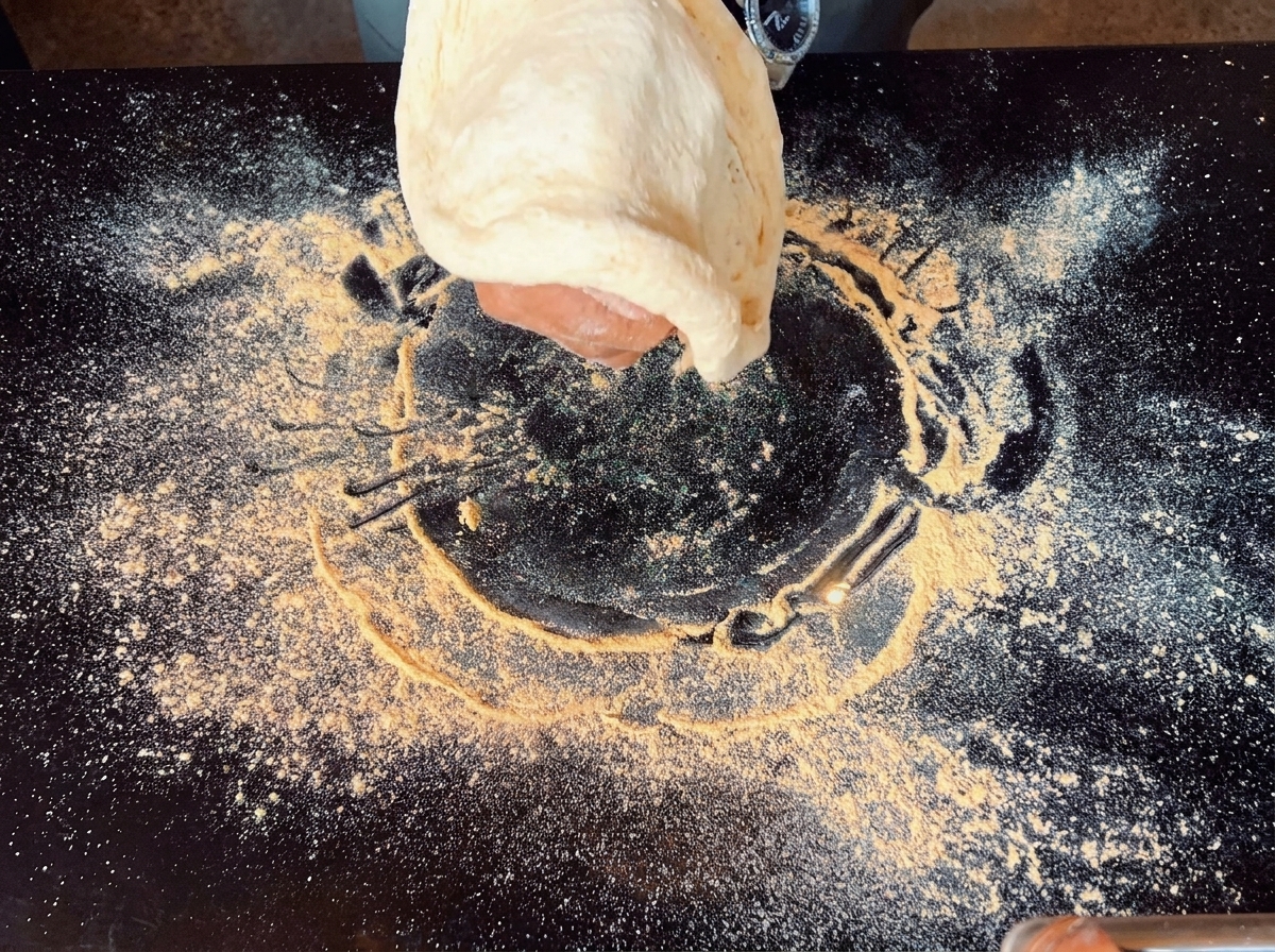 Eine Hand, die Pizzateig in der Luft über einer schwarzen Oberfläche dehnt.