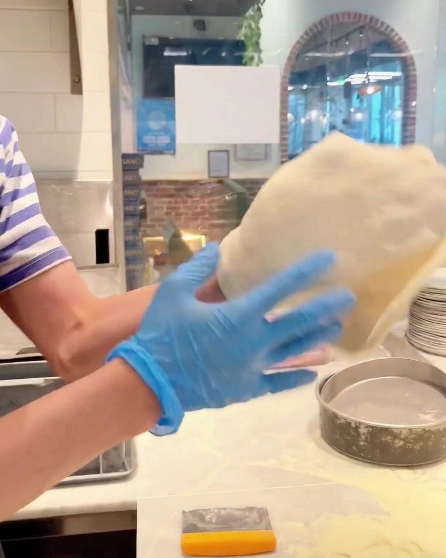 Hände rotieren einen Pizzateig, um ihn zu einem größeren Kreis zu dehnen.