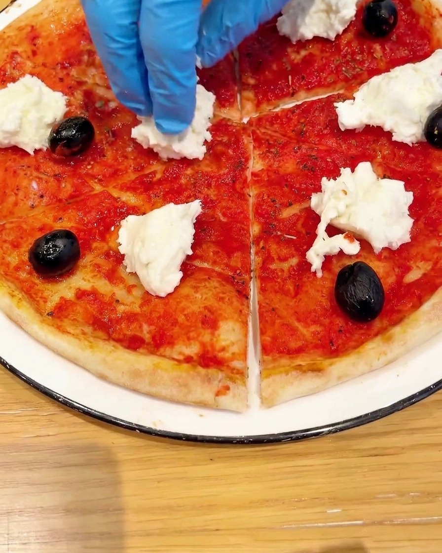 Draufsicht einer Pizza, die mit frischen Kirschtomatenhälften und grünem Basilikum garniert wird.