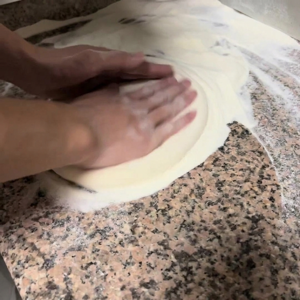 Hände drücken und dehnen den Pizzateig sanft auf einer bemehlten Arbeitsfläche.
