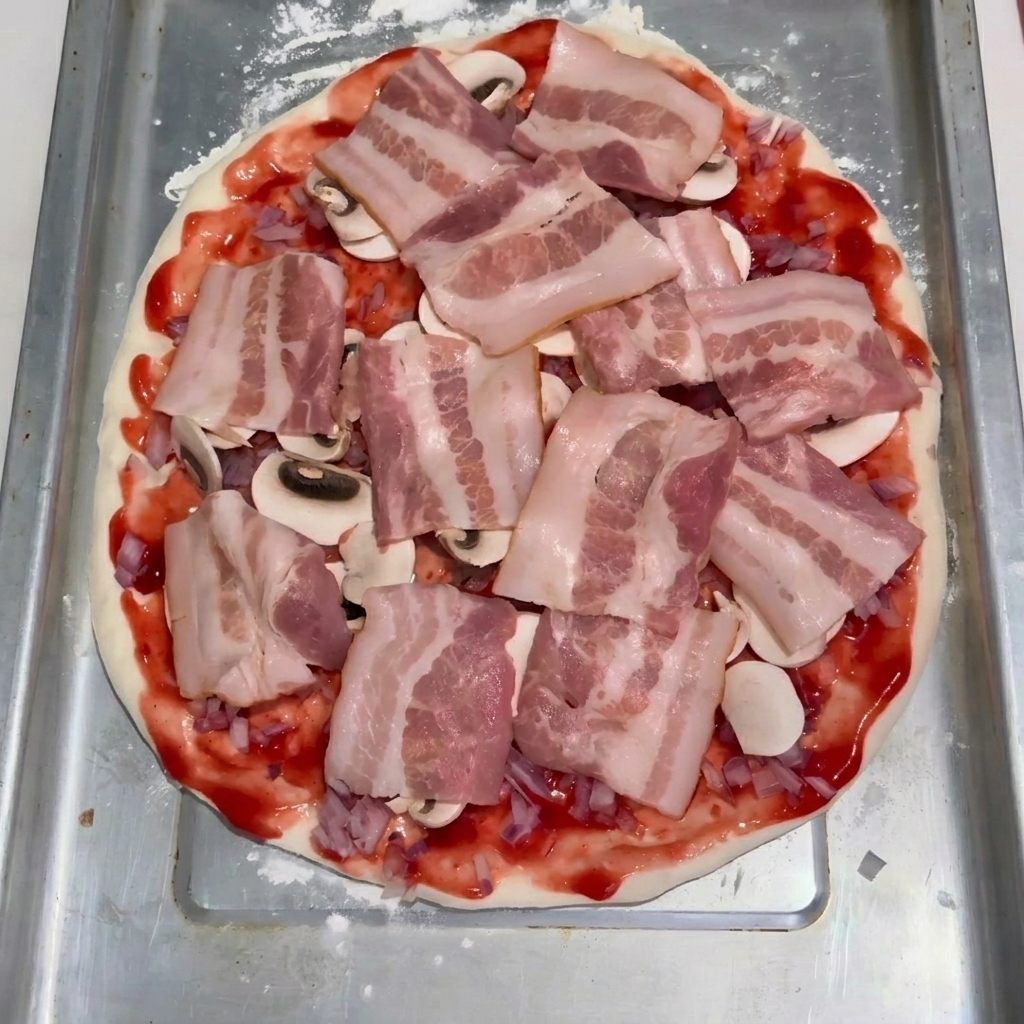 Speckscheiben liegen ordentlich über einer Schicht Pilze und Tomatensoße auf dem Pizzateig.