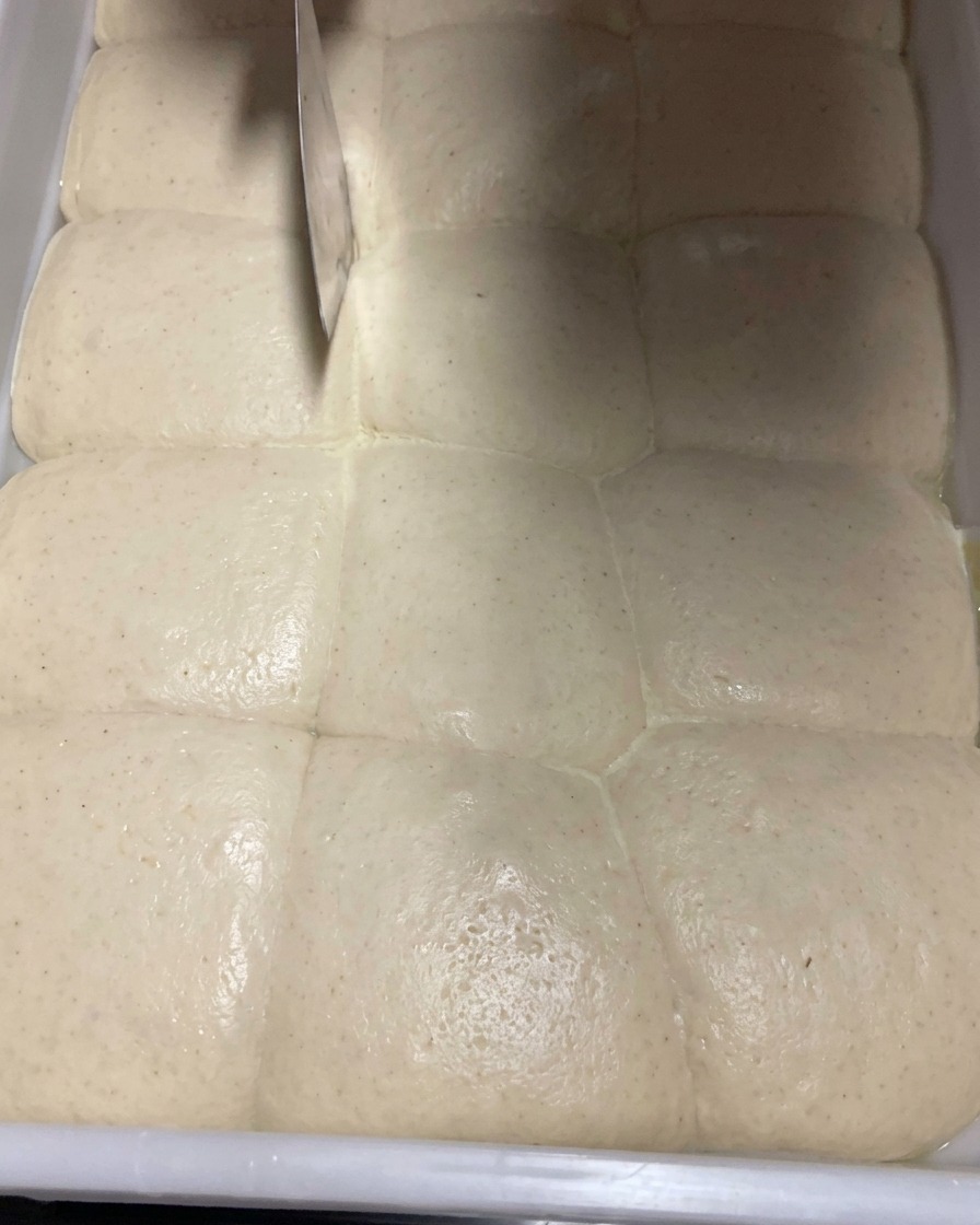 Nahaufnahme von fermentiertem Teig, der mit einem Teigteiler aus Metall vorsichtig in Portionen geteilt wird.