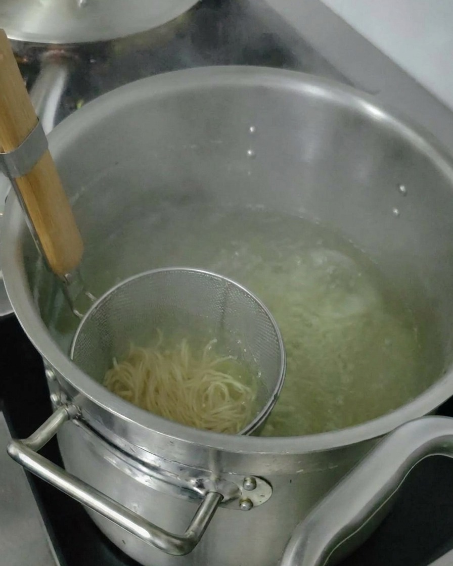 Gekochte Ramen-Nudeln werden im Sieb angehoben, um überschüssiges Wasser abtropfen zu lassen, bevor sie in die Schüssel gegeben werden.