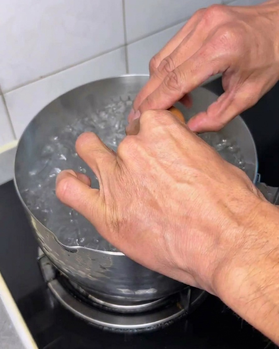 Ein rohes Ei wird in kochendes Wasser geschlagen.