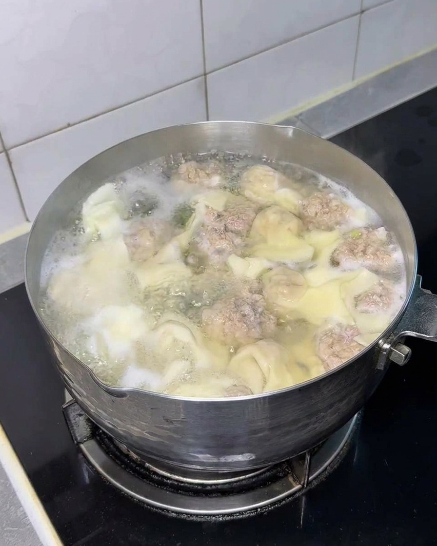 Ein Block Instant-Nudeln im Topf mit Wontons und Fleischbällchen.