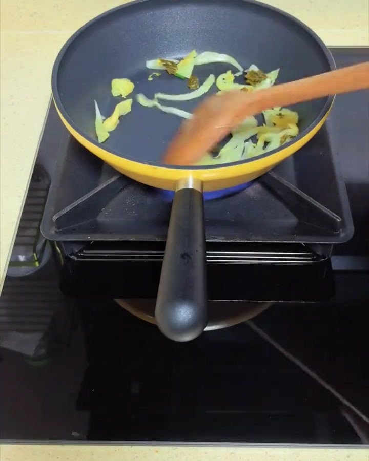 Eingelegtes Senfgrün wird in einer gelben Pfanne mit einem Holzspatel angebraten.