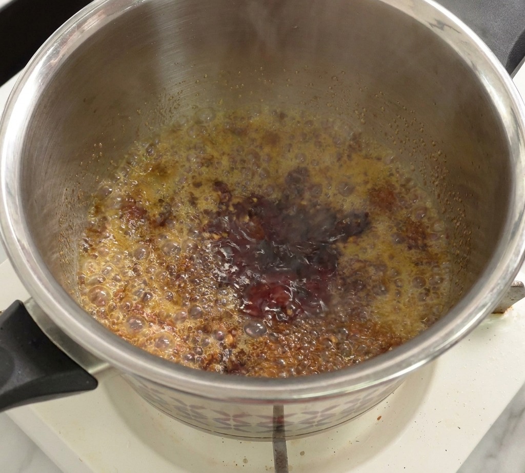 Eine Mischung aus Tomatensauce und Essig köchelt blubbernd in einem Topf.