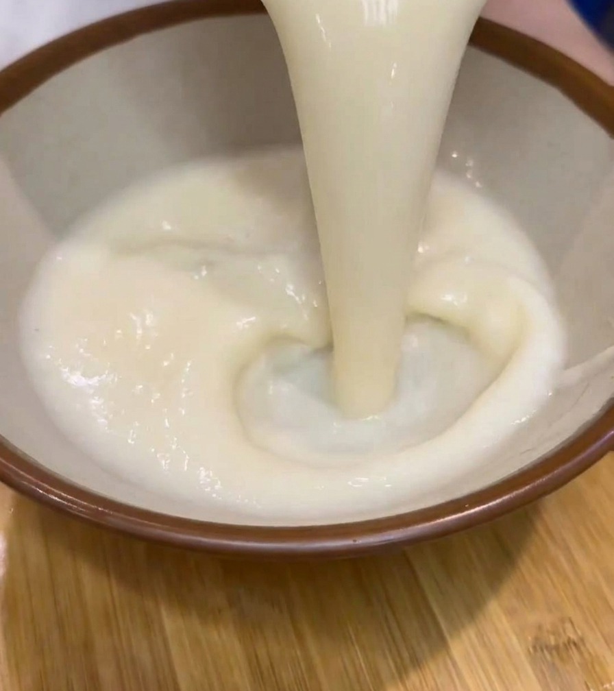 Dicke, cremige weiße Ramen-Suppe wird aus einem Krug in eine braun umrandete Keramikschale gegossen.
