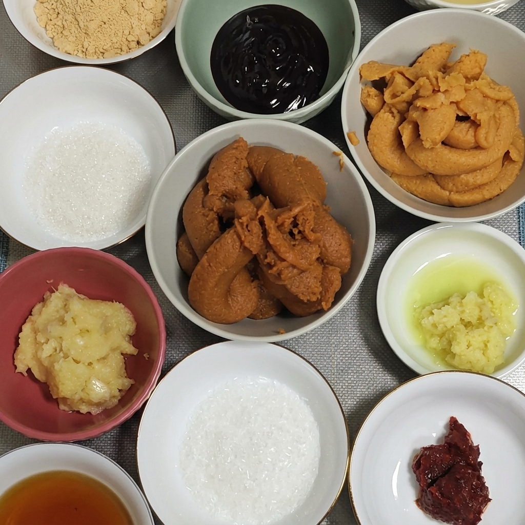 Ein großer Löffel mit dunkler, roter Miso-Paste wird in eine Schüssel mit Knoblauch und Ingwer gegeben.