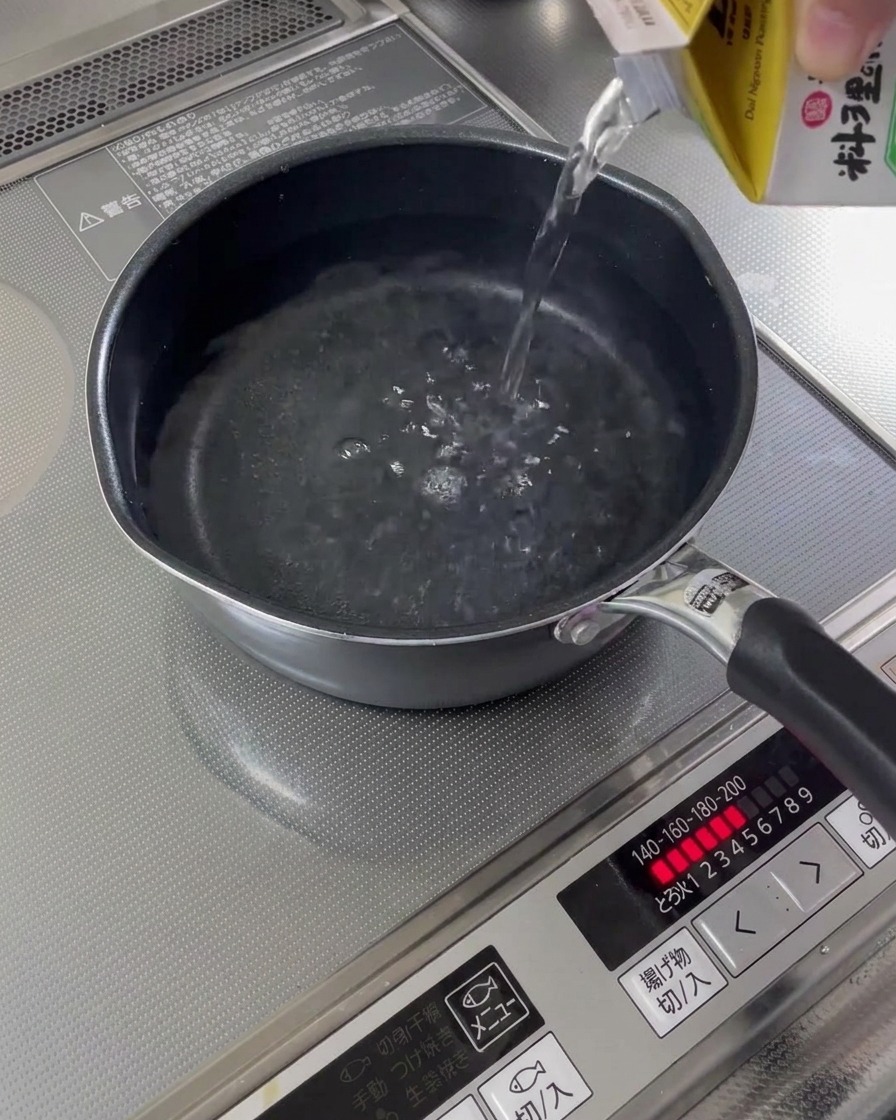 Wasser wird aus einem Karton in einen kleinen Topf auf dem Herd gegossen.