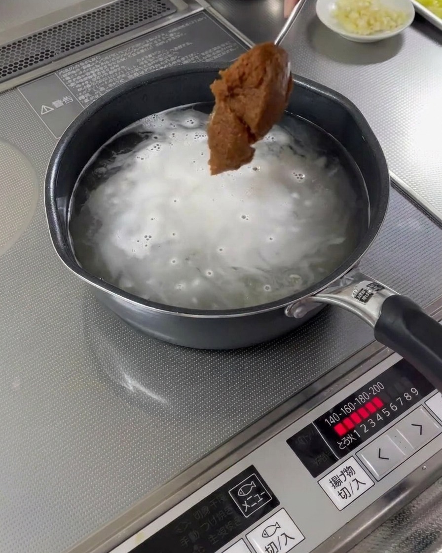 Ein Löffel Misopaste wird in eine kochende Brühe gegeben.