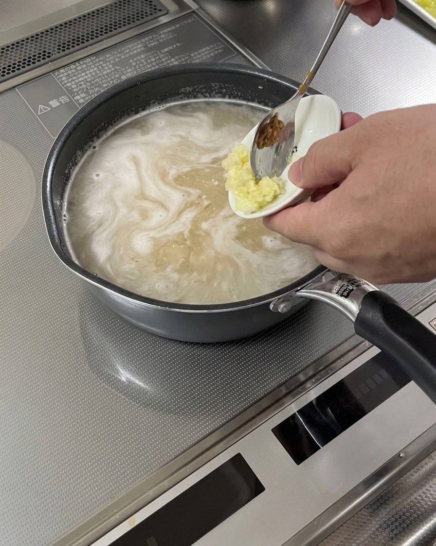 Geriebener Knoblauch und Ingwer werden in die köchelnde Suppenbasis gegeben.