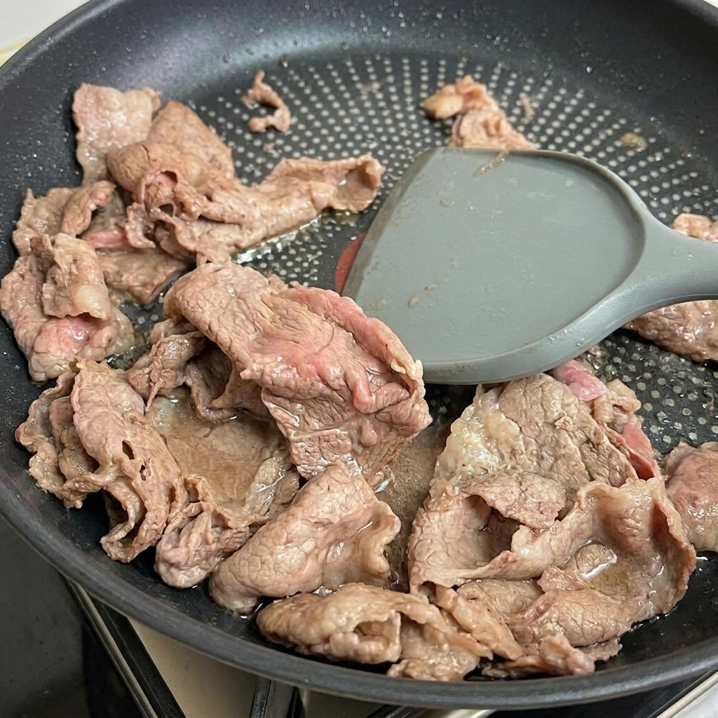 Zartes, leicht gebräuntes Rindfleisch wird mit einem Pfannenwender aus der Pfanne gehoben.