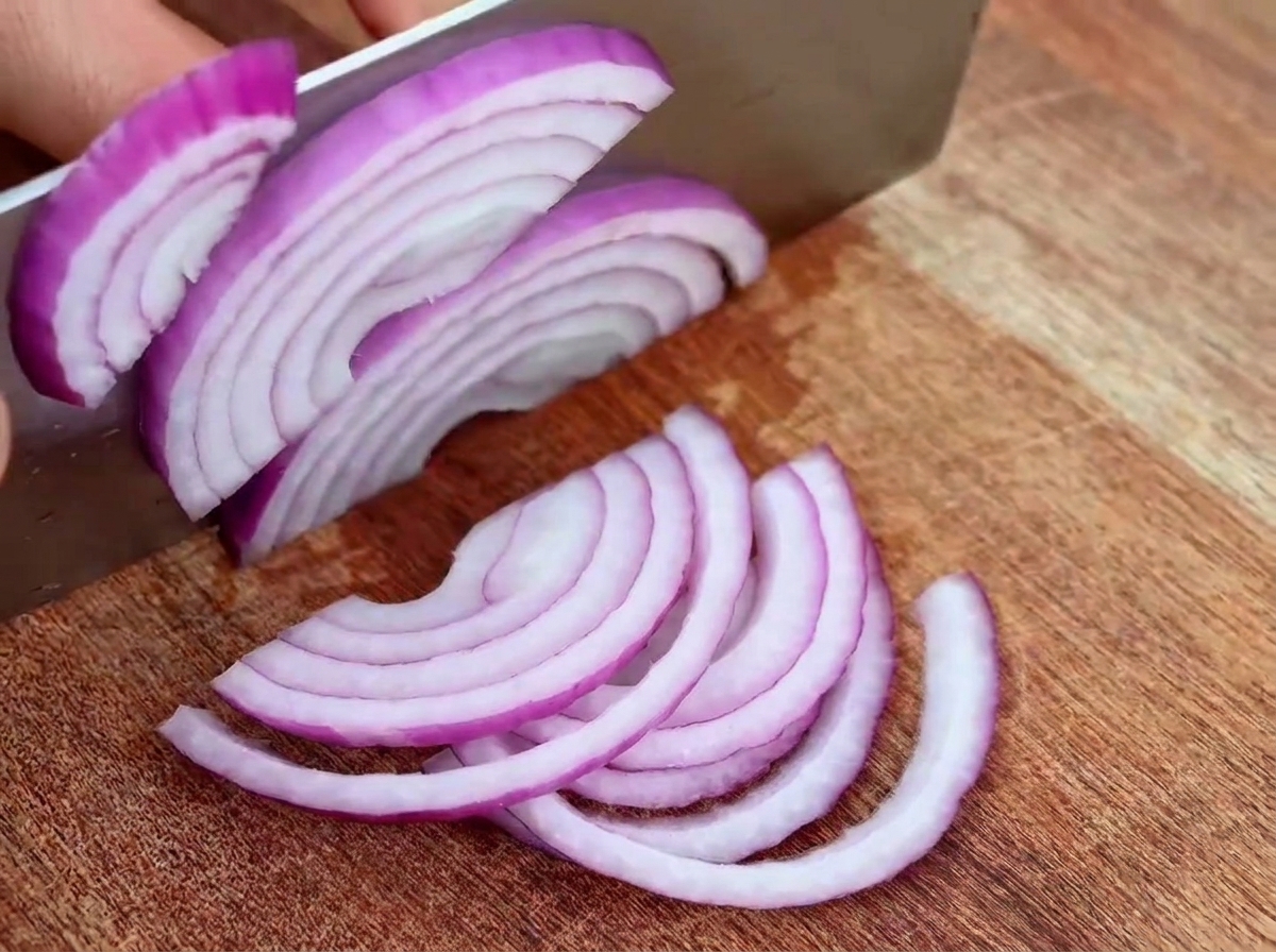 In halbe Ringe geschnittene rote Zwiebeln und Knoblauch auf einem Schneidebrett.
