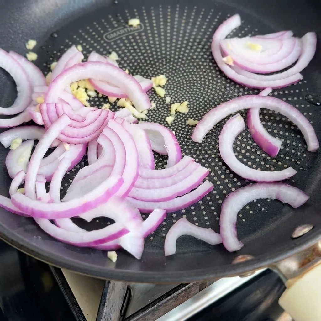 Zwiebeln und Knoblauch schmoren duftend in einer Pfanne.