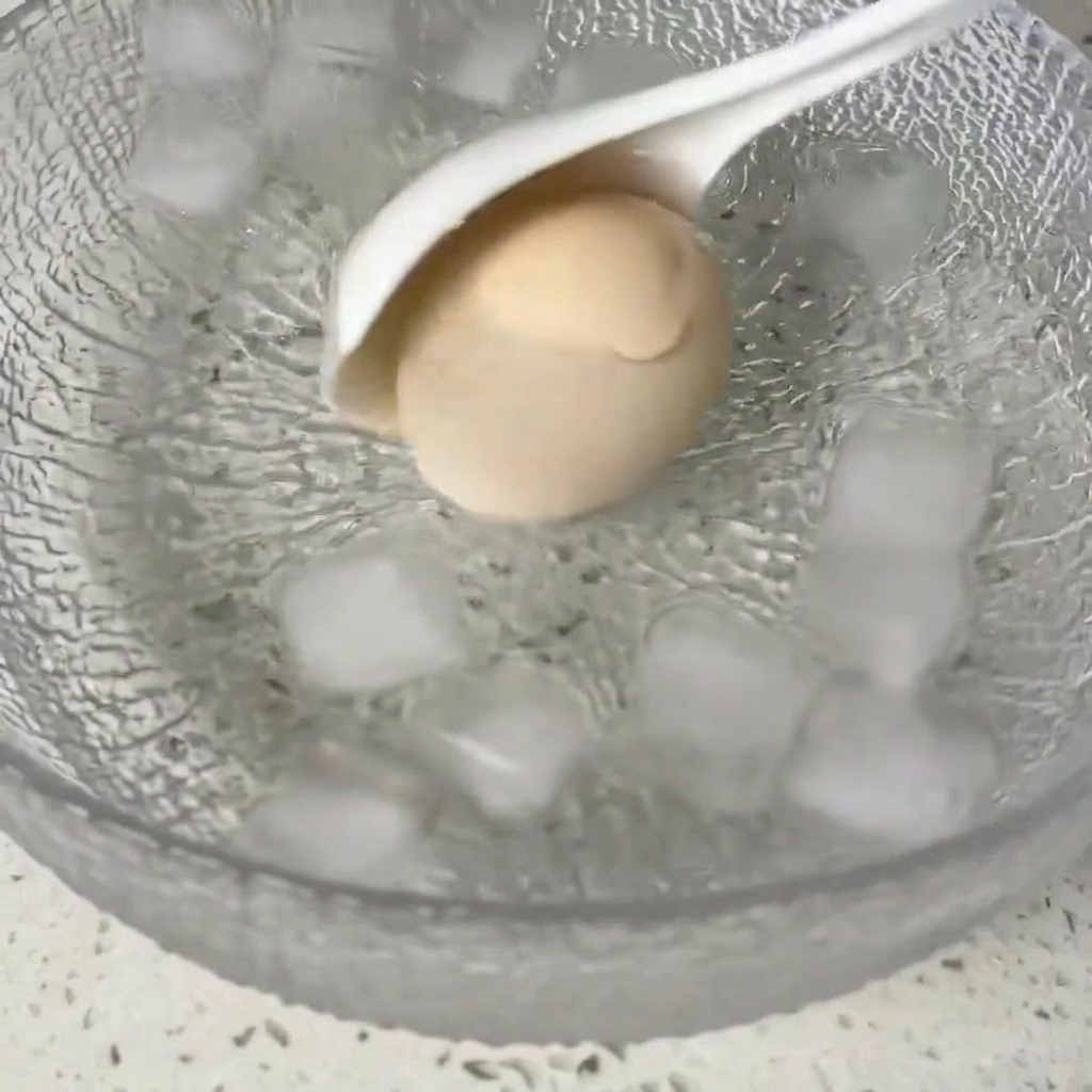 Ein gekochtes Ei wird in eine Schüssel mit Eiswasser gelegt.