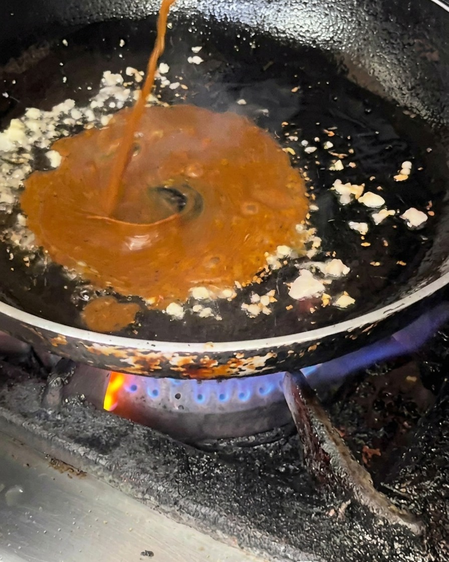 Dunkle Soße wird in eine Pfanne mit angebratenem Knoblauch und Zwiebeln gegossen.