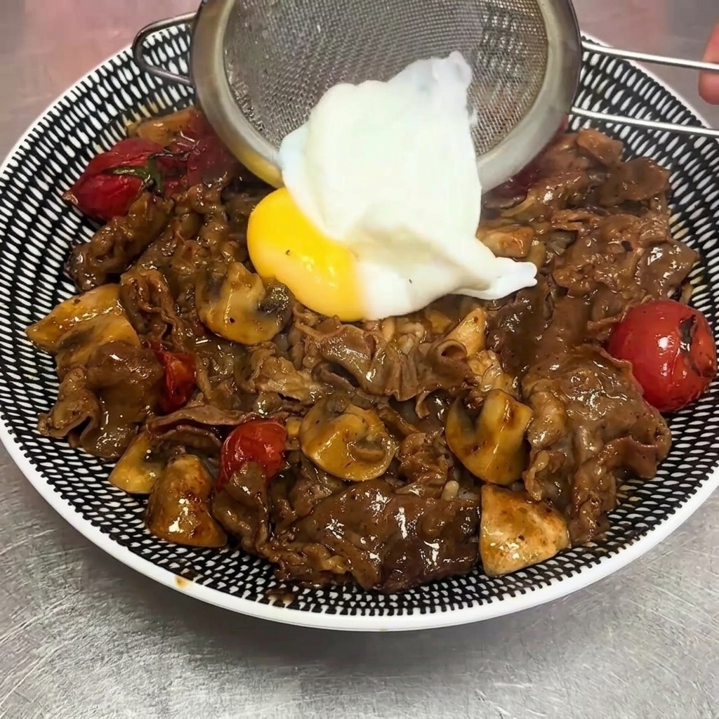 Ein weich gekochtes Ei wird mit einem Drahtsieb vorsichtig auf die Beef Rice Bowl gelegt.