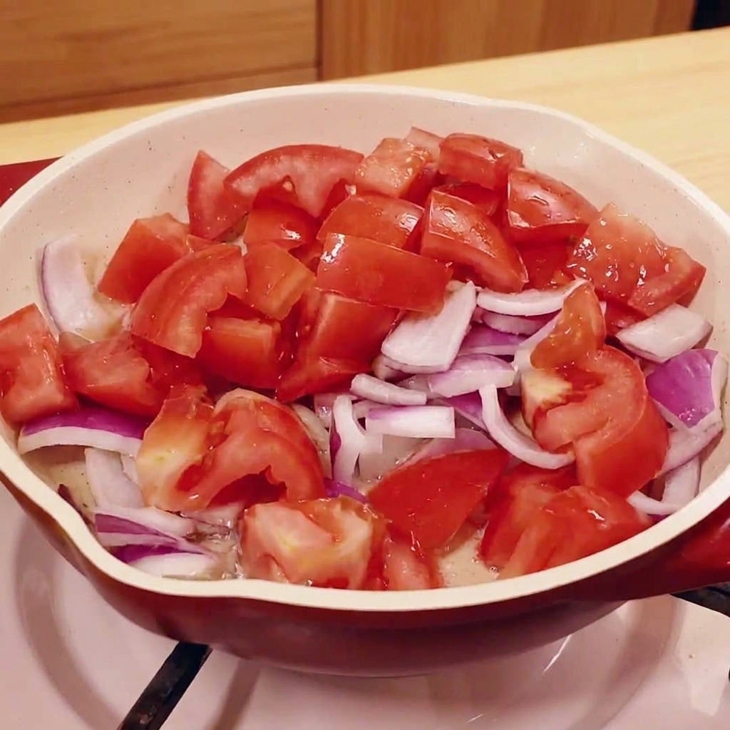 Gehackte Tomaten und rote Zwiebeln in einer Pfanne.