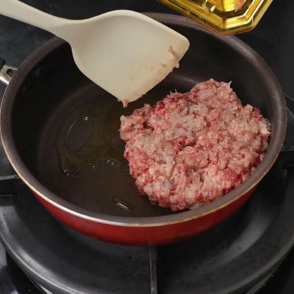 Rohes Hackfleisch wird in die geölte Pfanne gegeben und mit einem Pfannenwender zerkleinert.