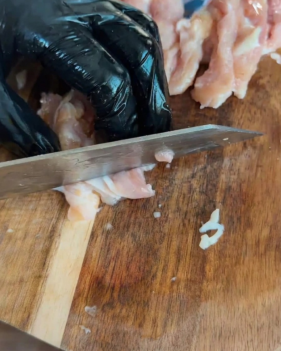 Gewürfelte rohe Hähnchenstücke auf einem Holzschneidebrett.