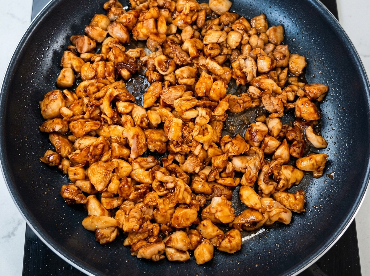 Gehackte Frühlingszwiebeln werden zum angebratenen Hähnchen in die Pfanne gegeben.