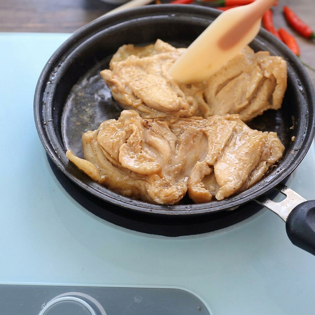 Angebratenes Hähnchen schmort in einer flachen Pfanne in dunkler Sauce.
