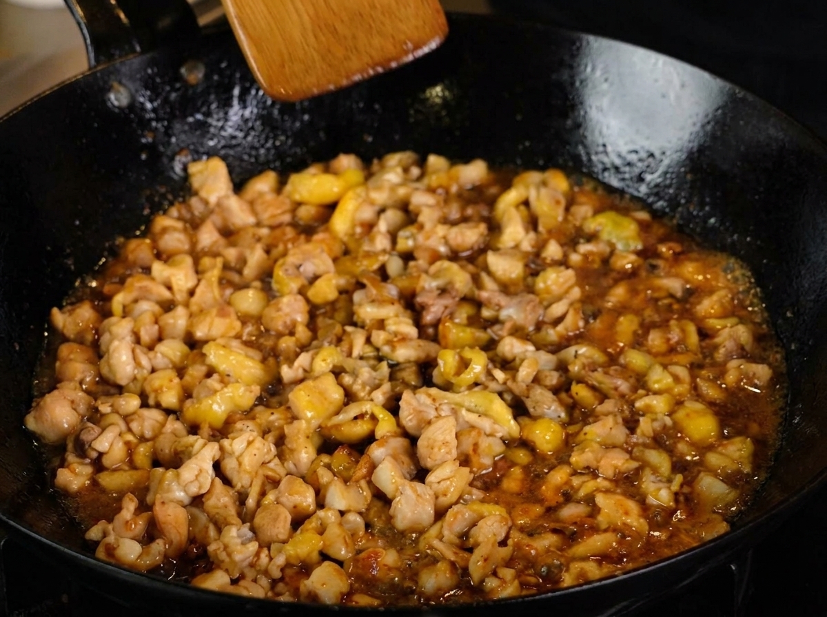 Das Hähnchen in dunkler Sauce köchelt in der Pfanne.