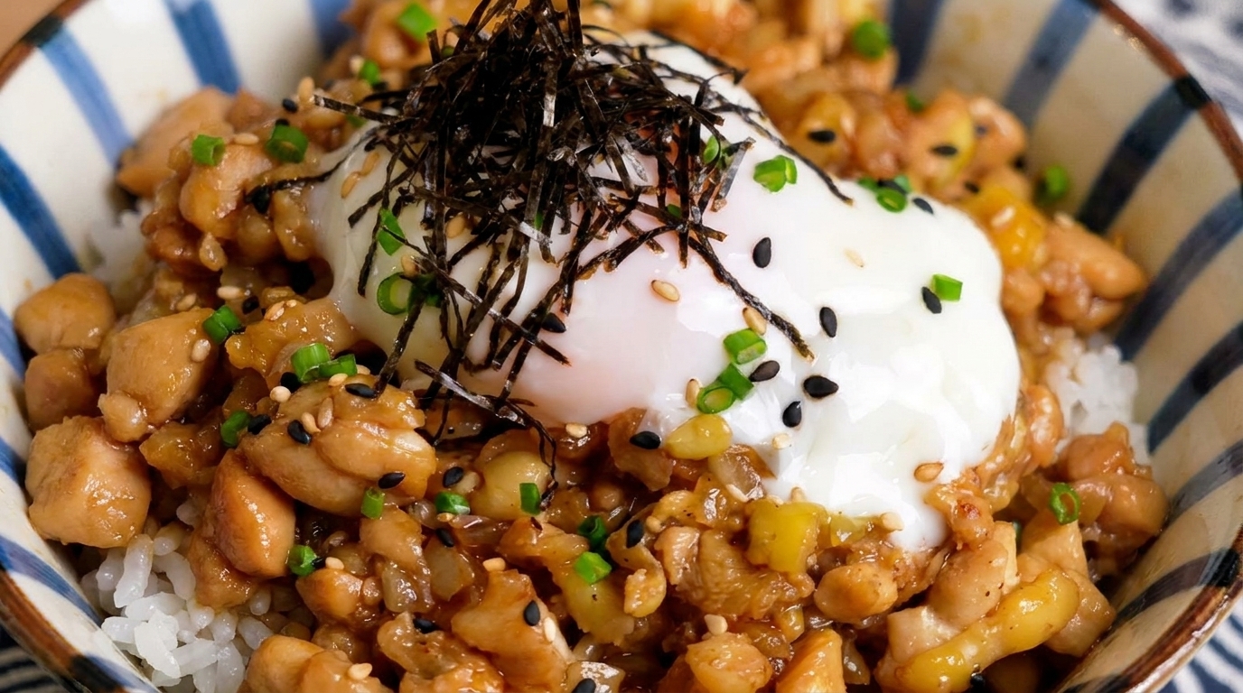 Eine Schale mit gehacktem Hähnchen auf Reis, garniert mit einem weichgekochten Ei, Nori-Streifen und Frühlingszwiebeln.