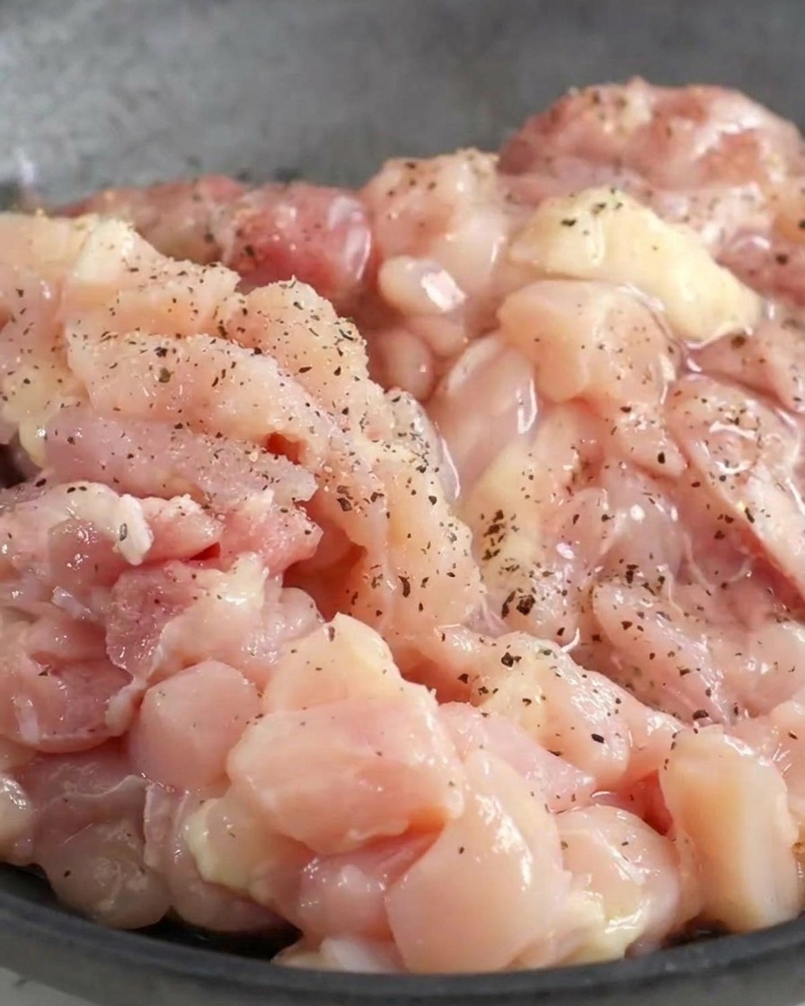 Gehacktes rohes Hähnchen in einer Schüssel, das mit schwarzem Pfeffer und flüssigen Gewürzen überzogen wird.
