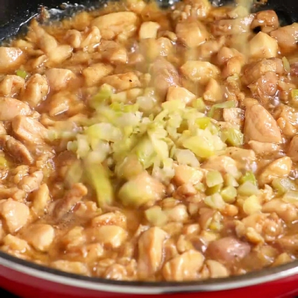 Fein gewürfelter eingelegter Senfkohl wird in eine Pfanne mit teilweise gegartem Hähnchenfleisch gegeben.