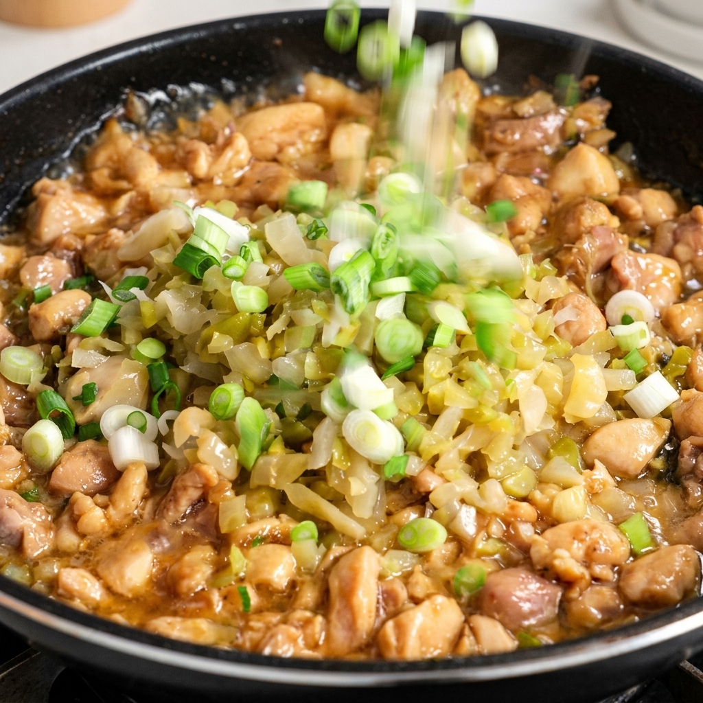 Gehackte weiße Teile von Frühlingszwiebeln werden in eine Pfanne mit Hähnchen und eingelegtem Kohl gestreut.