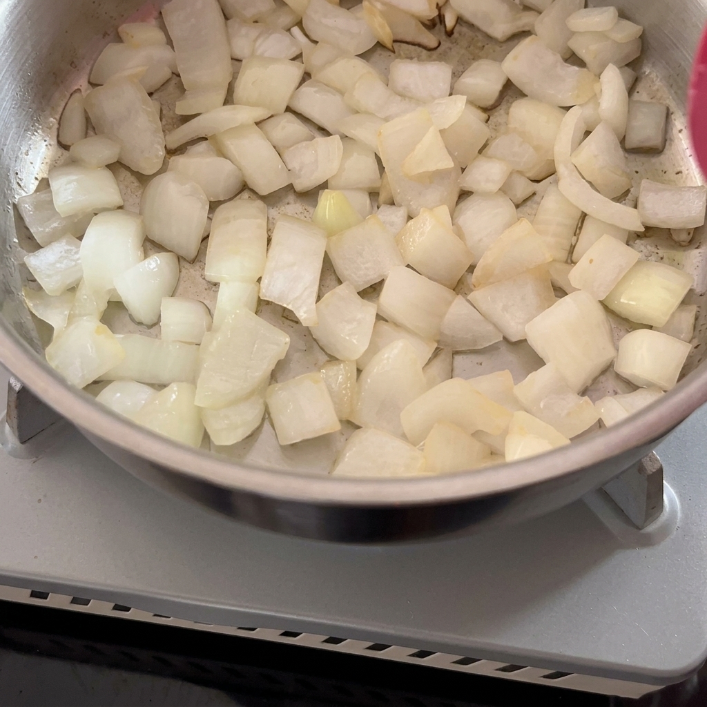 Gehackte Zwiebeln in einem Metalltopf beim Anschwitzen.