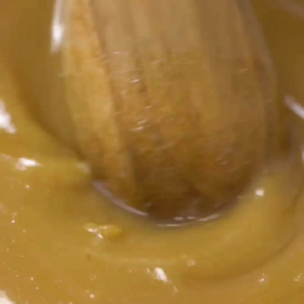 Ein Holzlöffel rührt die goldbraune Miso-Marinade in einer Glasschüssel glatt.