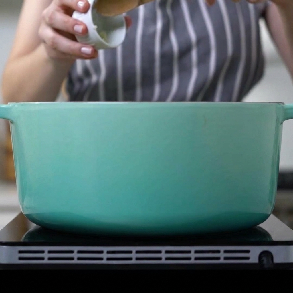 Gehackter Knoblauch wird in einen Topf mit angebratenen Schweinerippchen und Zwiebeln gegeben.