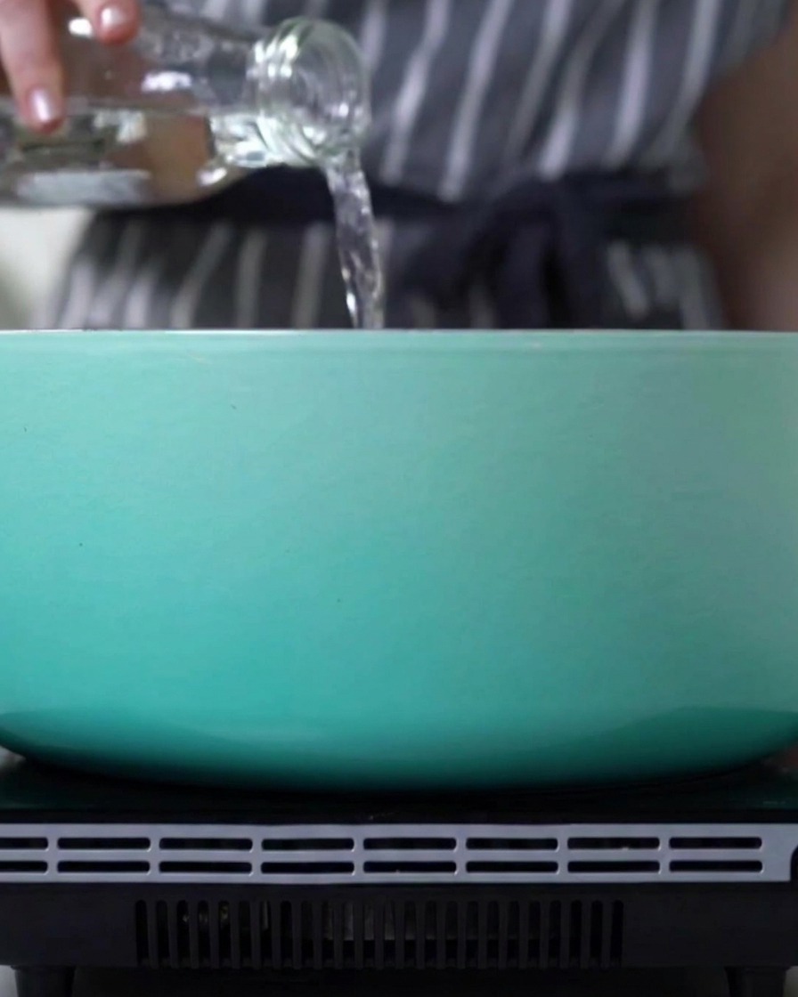 Wasser wird aus einer Glasflasche in einen Topf auf dem Herd gegossen.