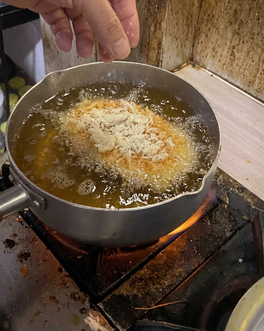 Ein paniertes Schweineschnitzel wird vorsichtig in einen Topf mit heißem Frittieröl gelassen.