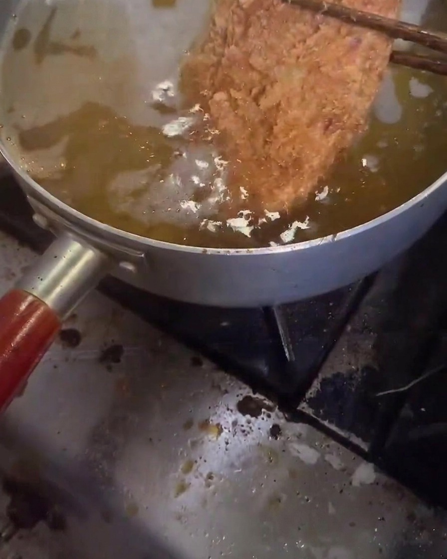 Ein Schnitzel wird zum zweiten Mal in heißem Öl frittiert.