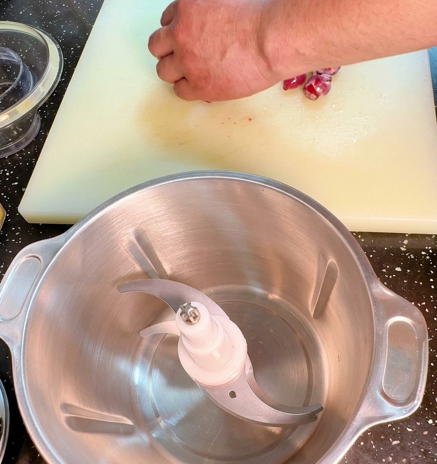 Eine Nahaufnahme einer Hand, die eine rote Zwiebel mit einem großen Kochmesser auf einem weißen Schneidebrett fein würfelt.