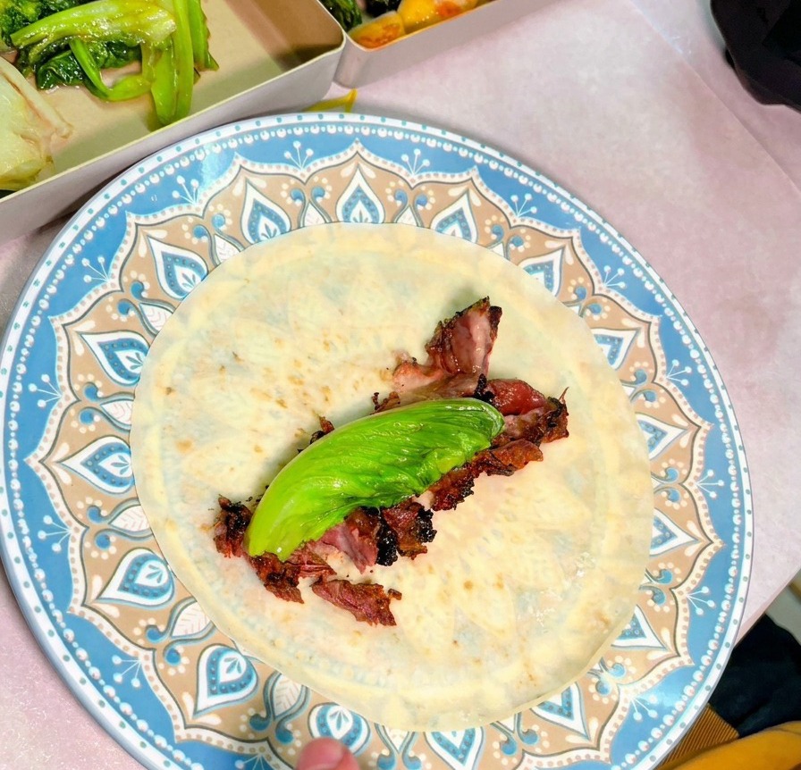 Draufsicht auf einen blau gemusterten Teller mit einer Tortilla, belegt mit saftigen Scheiben Smoked Beef und einem frischen grünen Blatt.