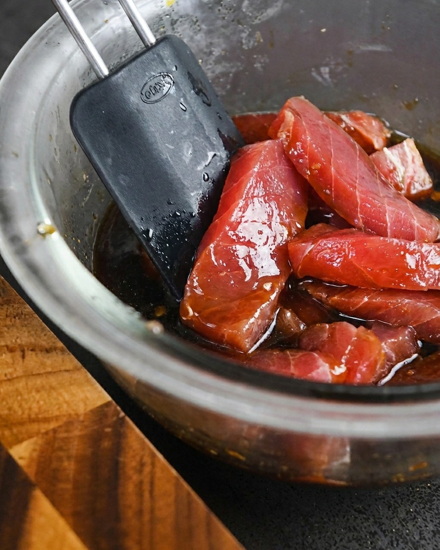 Dicke Stücke roher Thunfisch werden mit einem Spatel in einer dunklen Marinade vermengt.