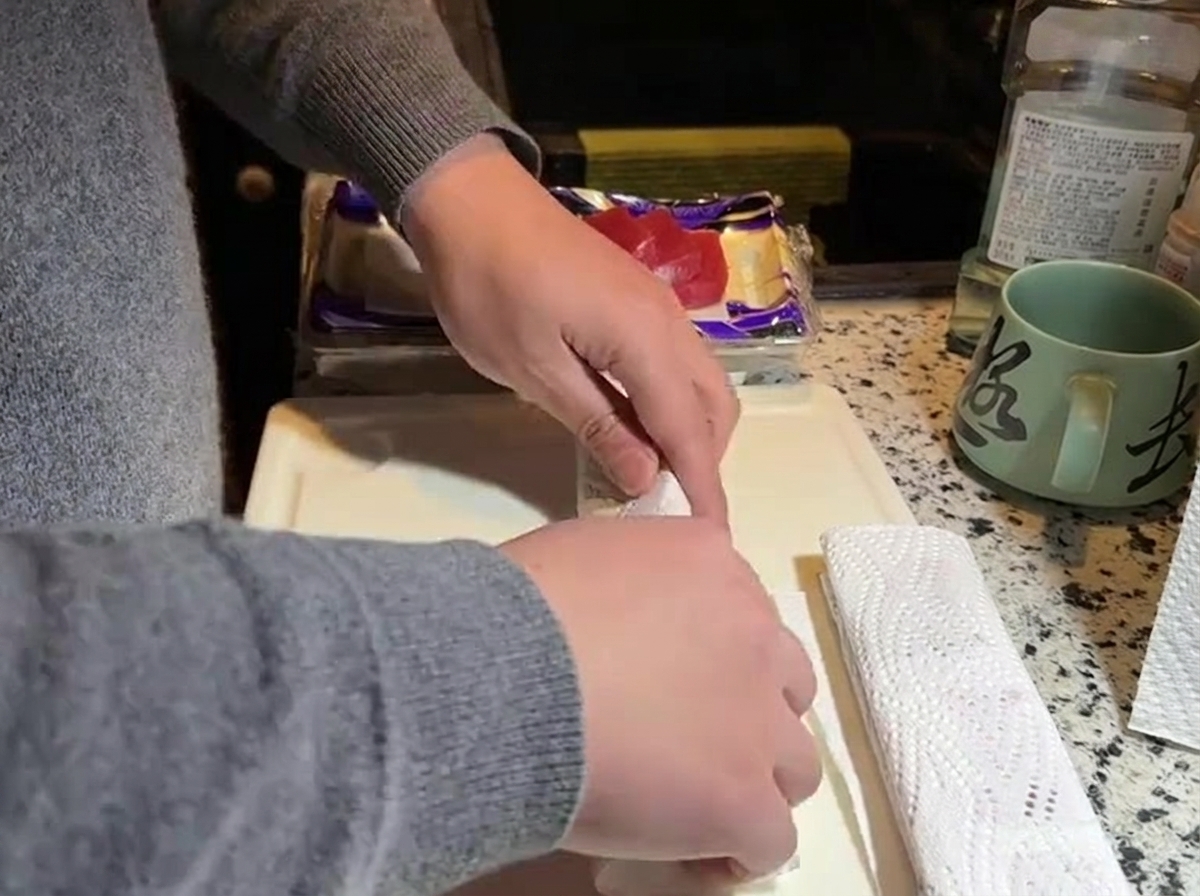 Hände drücken weißes Küchenpapier auf einen Block rohen Thunfisch auf einem weißen Schneidebrett.