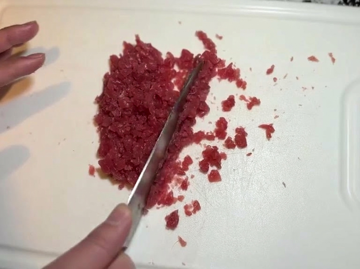 Ein Messer beim feinen Würfeln und Hacken von rohem Thunfisch auf einem Schneidebrett.