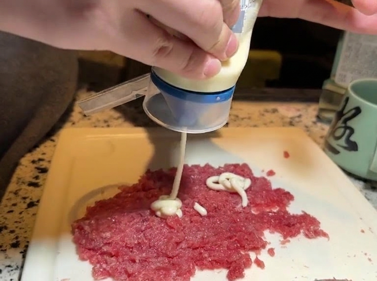 Weiße Mayonnaise wird aus einer Flasche auf einen Teil des gehackten Thunfischs gedrückt.