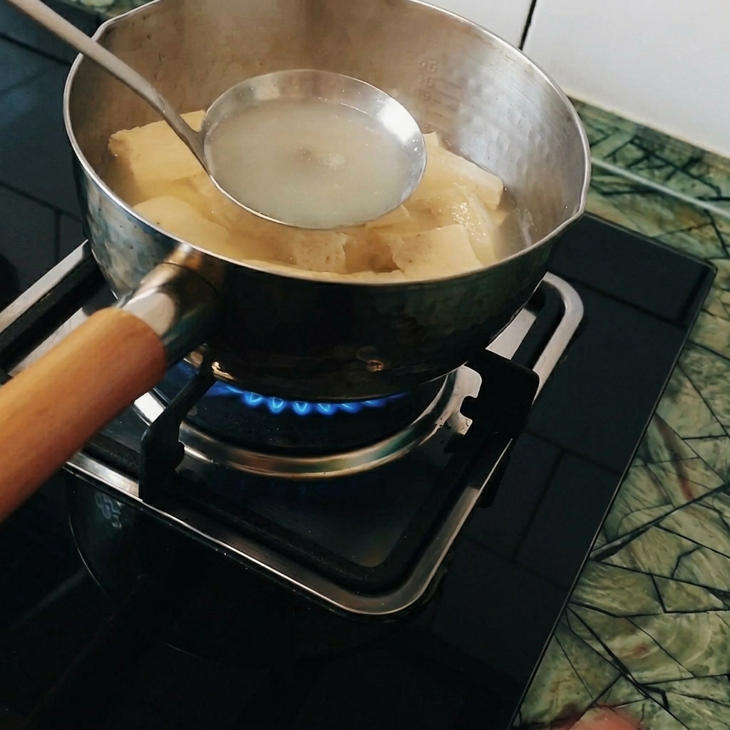 Currystücke werden in einer Schöpfkelle innerhalb eines Topfes mit kochendem Wasser aufgelöst.