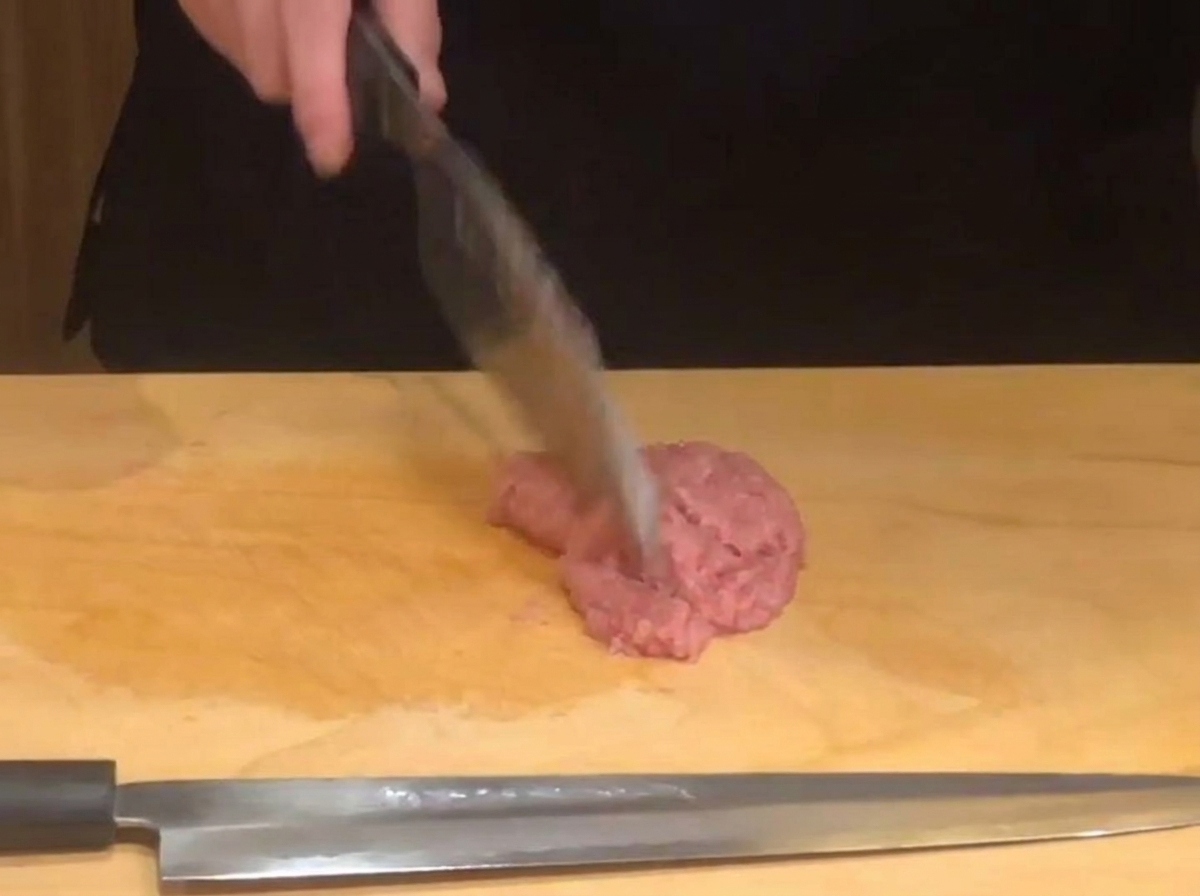 Ein Messer zerkleinert frischen Thunfisch auf einem Holzbrett.