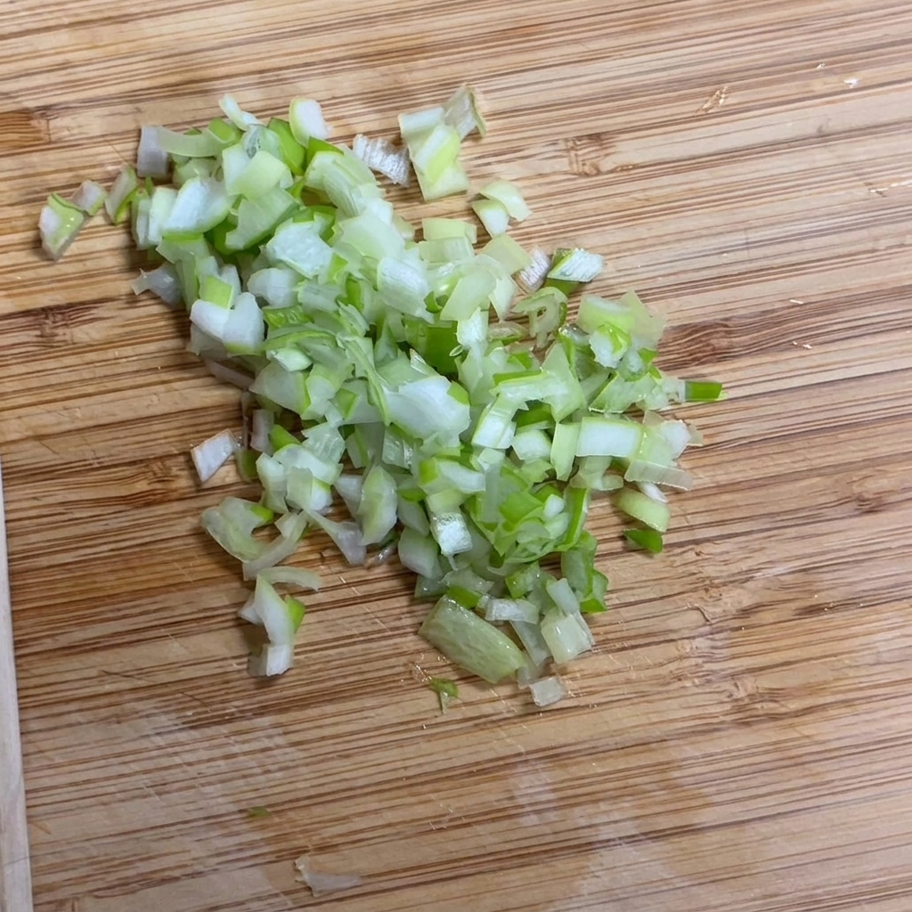 Frische Frühlingszwiebeln werden auf einem Holzbrett fein gehackt.