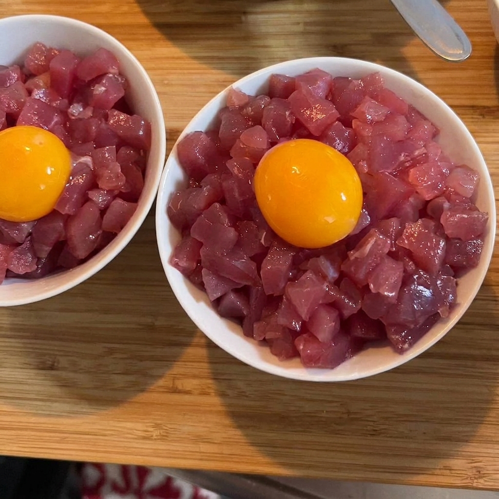 Ein leuchtend gelbes Eigelb ruht in der Mitte einer Schale mit Thunfisch und Reis, bestreut mit grünen Frühlingszwiebeln.